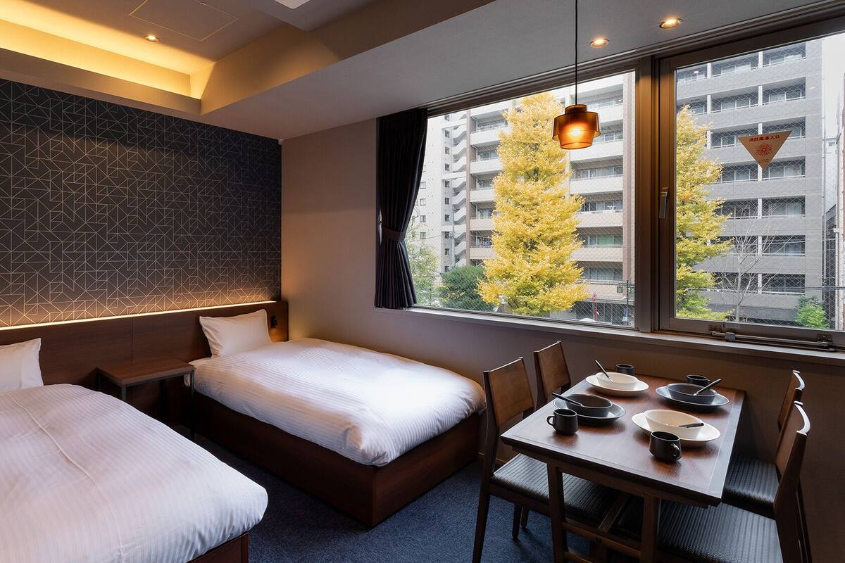 Een hotelkamer met twee bedden, een eettafel met stoelen en uitzicht op een stadsbeeld.