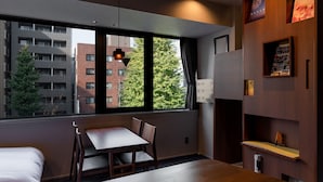 A modern hotel room with a large window, a wooden dining table, and a built-in bookshelf. - COCOSHUKU Shinjuku-Hanazono (Tokyo)