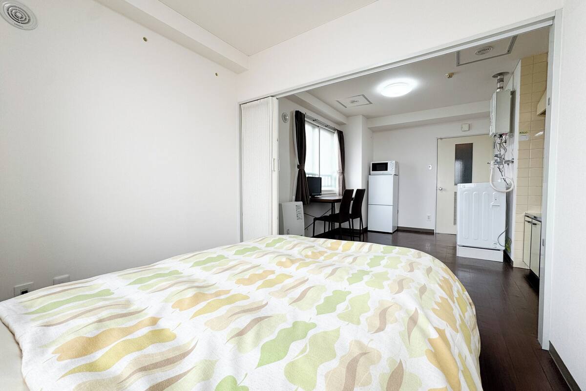 A hotel room with a bed, a desk, a refrigerator, and a shower area.
