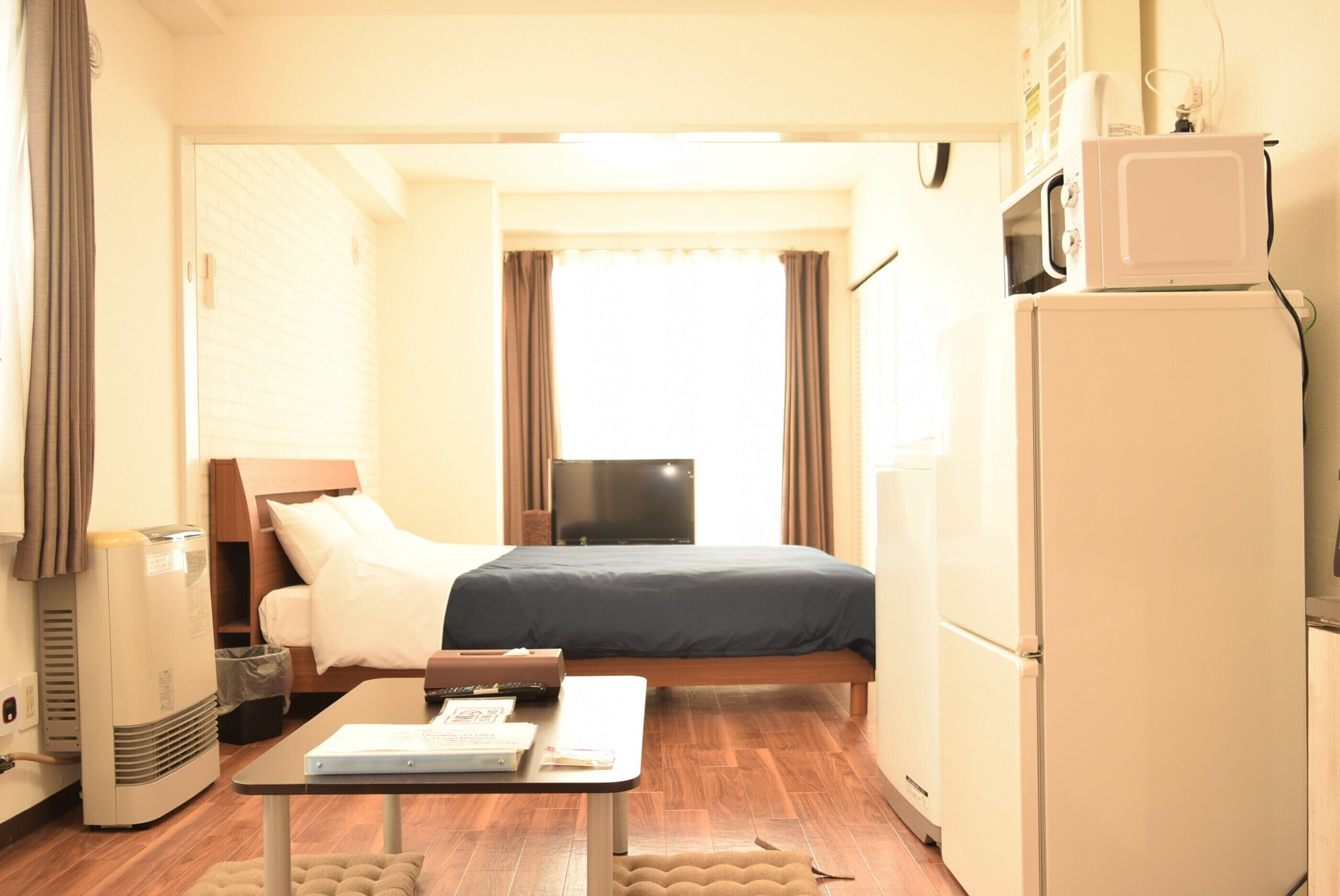 A compact hotel room with a bed, a small table, a refrigerator, and a television.
