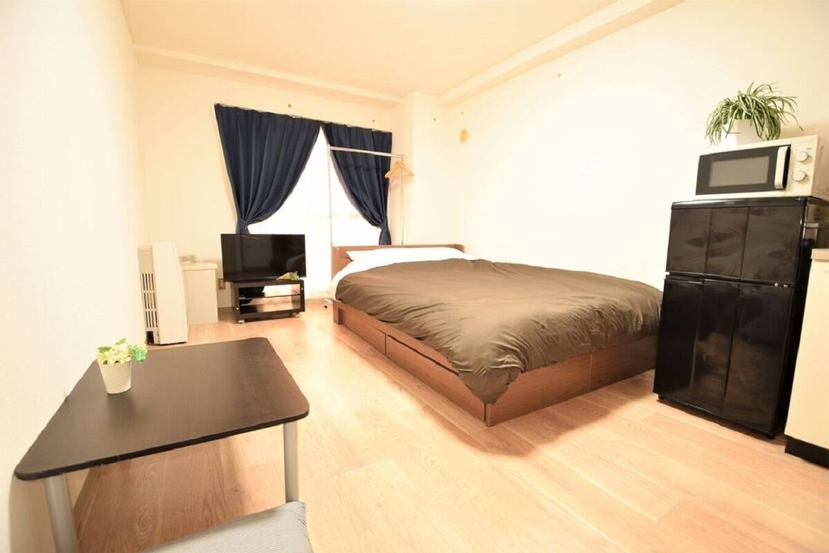 A compact bedroom with a bed, a small desk, a TV, a microwave, and a refrigerator.