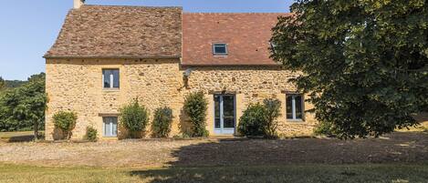 A stone house with a tiled roof, a small window, and a door.