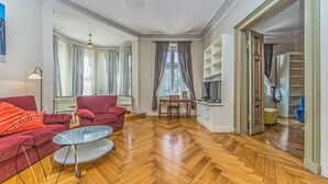 Un vaste espace de vie doté d’un parquet en bois disposé en point de Hongrie, d’un canapé rouge, d’une table basse en verre et d’un coin repas comprenant une chaise et une table.