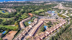 An aerial view of a coastal resort with multiple buildings, a large swimming pool, and surrounding greenery.