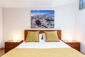 Ein Schlafzimmer mit einem Bett, zwei Nachttischen und einem an der Wand hängenden Bild von einer Strandansicht.