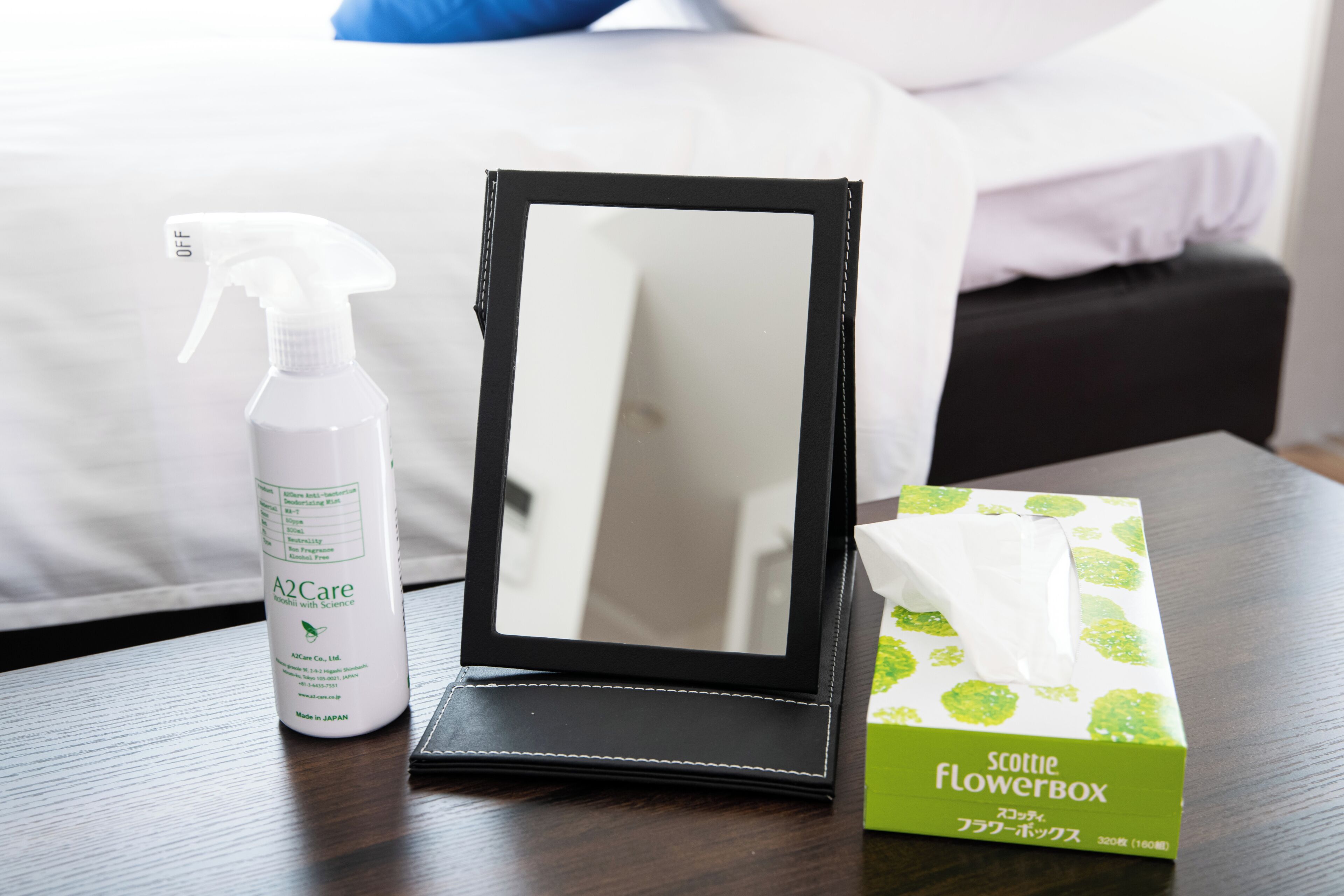 A bedside table with a black mirror, a bottle of A2Care spray, and a tissue box.
