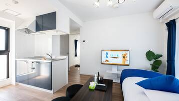 A modern kitchen with a built-in stove, a dining area with a wooden table, and a living room with a sofa and a TV.