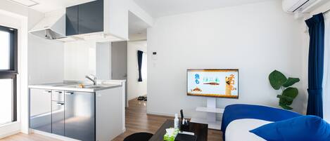 A modern kitchen with a built-in stove, a dining area with a wooden table, and a living room with a sofa and a TV.