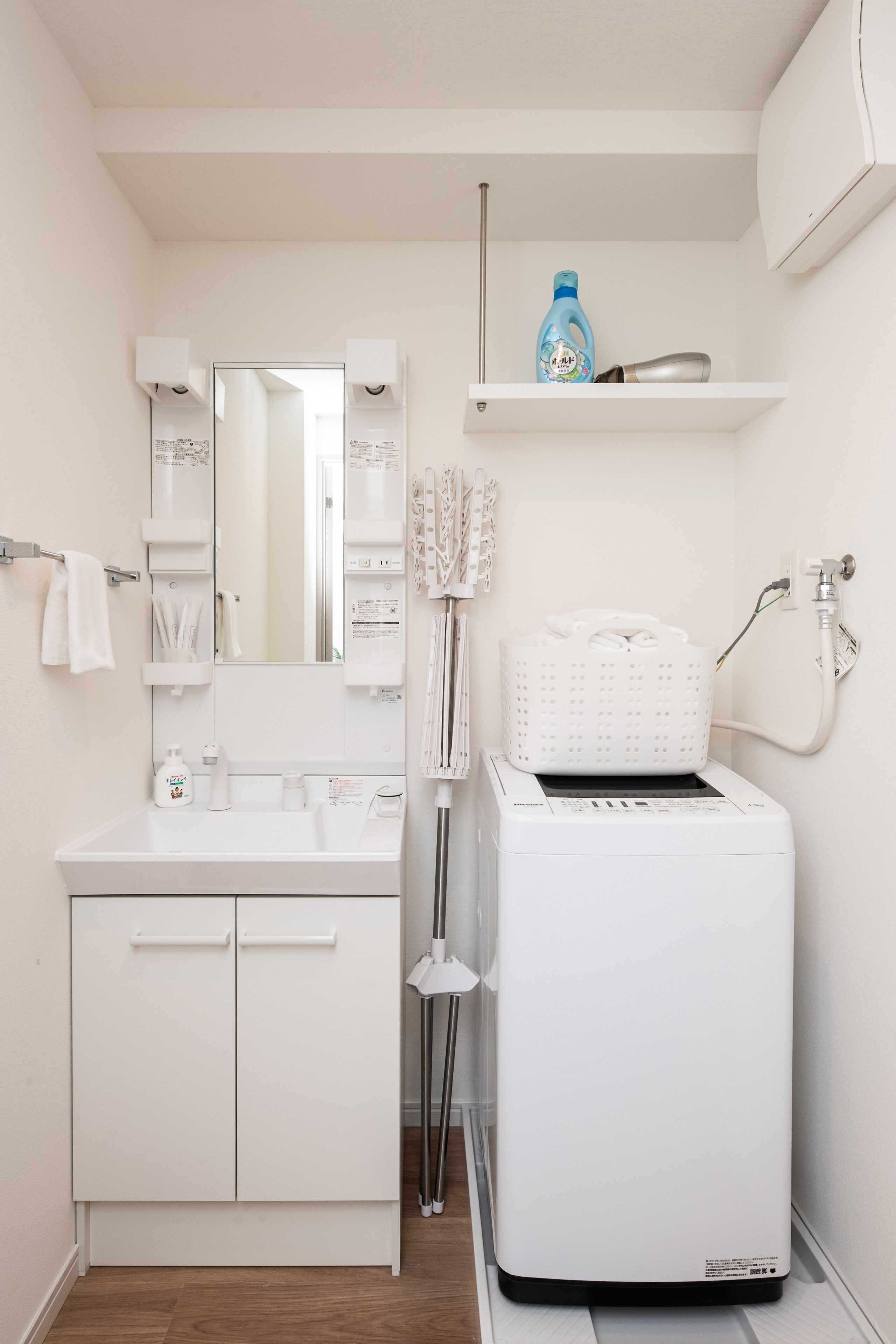 Un baño moderno con tocador blanco, un espejo grande, una lavadora blanca y un estante con artículos de aseo.