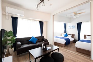 Ein modernes Hotelzimmer mit einer Couch, zwei Betten, einem Couchtisch und einer Klimaanlage.