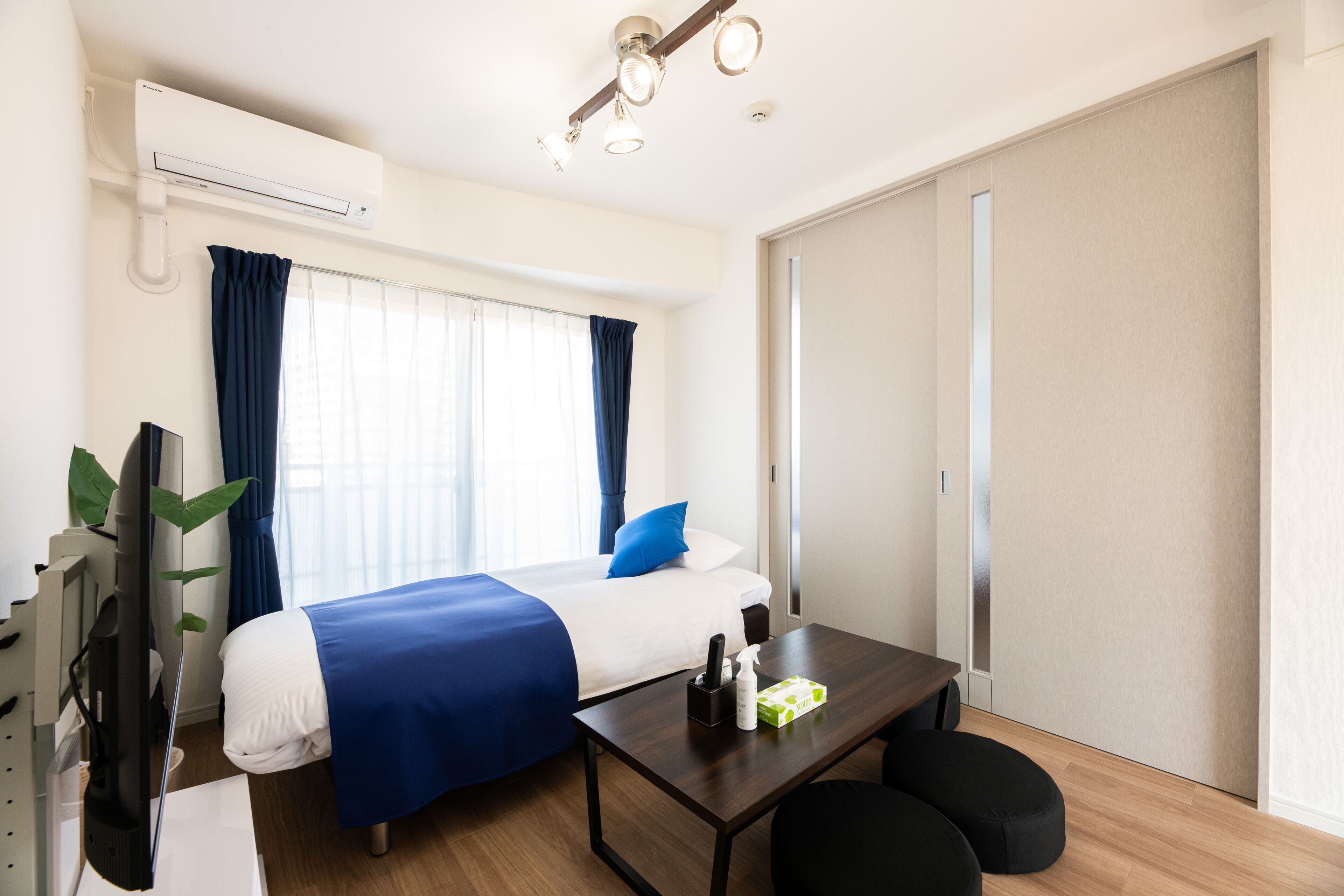 Una habitación de hotel con cama, escritorio, silla, televisor y aire acondicionado.