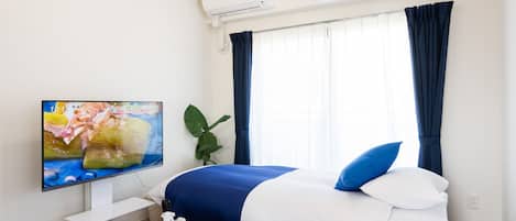 Une chambre d’hôtel avec un lit, une télévision, une table avec un coffre et des poufs noirs.