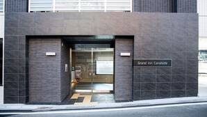 Une entrée d’hôtel moderne avec une porte en verre, une plaque indiquant le nom « Grand Inn Canalside », et un extincteur bien visible.