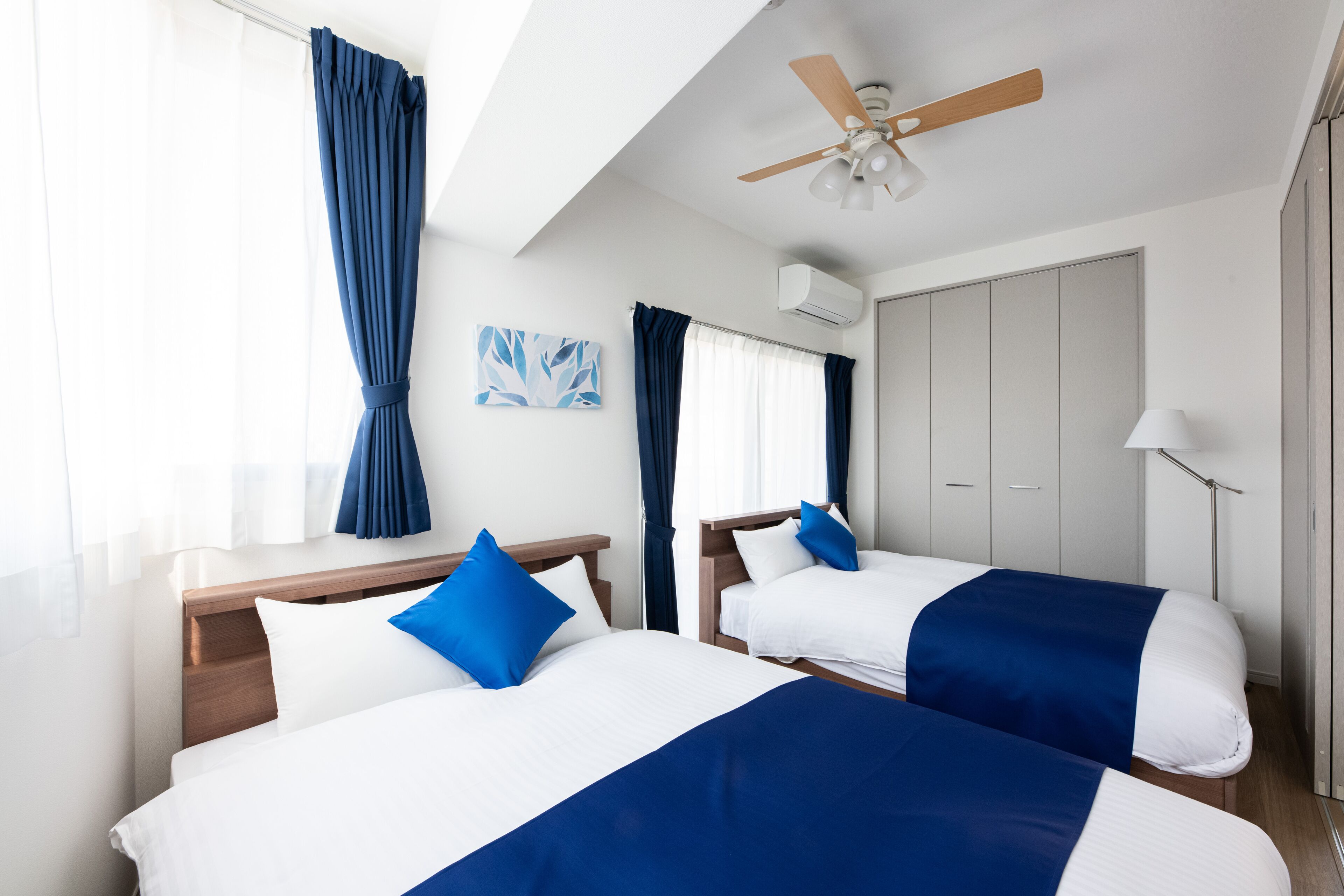 Een hotelkamer met twee bedden, een plafondventilator, een raam met gordijnen en een deur.