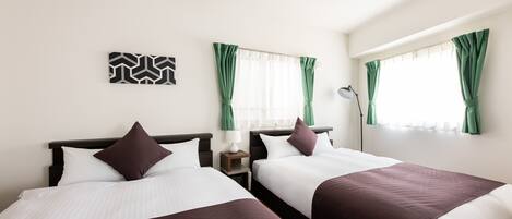 A hotel room with two beds, a ceiling fan, a nightstand with a lamp, and a window with green curtains.