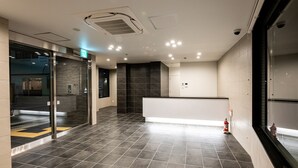 Un hall d’hôtel moderne avec un comptoir d’accueil, des portes vitrées et un sol carrelé.