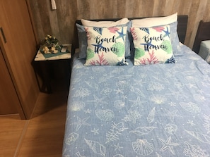 Una cama con colcha azul adornada con motivos de criaturas marinas blancas y dos almohadas con el texto 'Beach Heaven'.