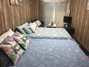 A hotel room with two beds, each with a blue floral bedspread and multiple pillows. There is a small table with a plant and a TV on a stand. - Beach Lodge 2 & Private Beach (Onna)