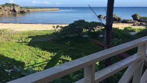 A view from a balcony overlooking a beach with a wooden railing, lush greenery, and the ocean. - Beach Lodge 2 & Private Beach (Onna)