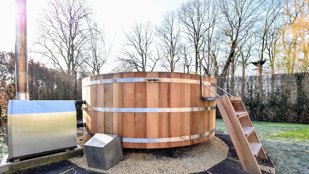 A wooden hot tub with a metal ladder and a metal grill on a circular platform with black and white tiles. - Spacious Holiday Home in Rekken With Hot Tub (Rekken)