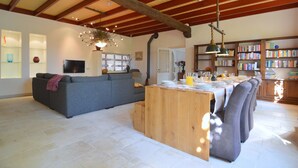 A spacious living area with a sofa, a wooden dining table set for a meal, and a bookshelf filled with books. - Spacious Holiday Home in Rekken With Hot Tub (Rekken)