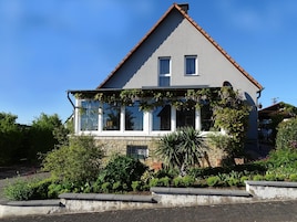 A two-story house with a balcony, stone foundation, and a red-tiled roof.