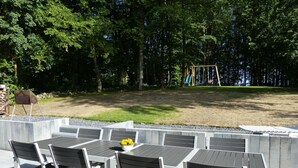 Un área de estar al aire libre con una jardinera de concreto, una parrilla y una estructura de juegos para niños al fondo.