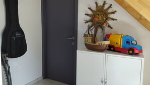 Una habitación con una puerta oscura, un armario blanco, una guitarra colgada en la pared, y un barco decorativo y un camión sobre el armario.