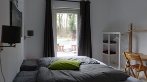 Un dormitorio con cama, escritorio, silla, televisor y ventana con cortinas.