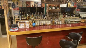 A bar area with a wooden counter, various liquor bottles, and two black bar stools. - Beach Lodge 4 & Private Beach (Onna)