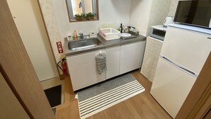 A compact kitchen with a stainless steel sink, a microwave, and a refrigerator. There is a window above the sink with plants on the windowsill, and a small window with frosted glass. - Beach Lodge 4 & Private Beach (Onna)