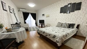 A bedroom with a bed, a desk, a chair, a TV, and a window with curtains. - Beach Lodge 4 & Private Beach (Onna)