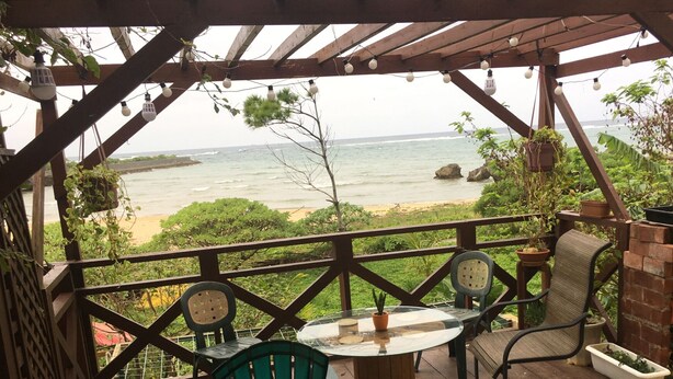 A covered outdoor seating area with a view of the ocean, featuring a brick barbecue, potted plants, and a round table with chairs. - Beach Lodge 4 & Private Beach (Onna)