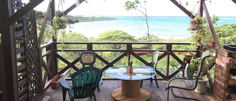 A covered patio with a table and chairs, overlooking a body of water.