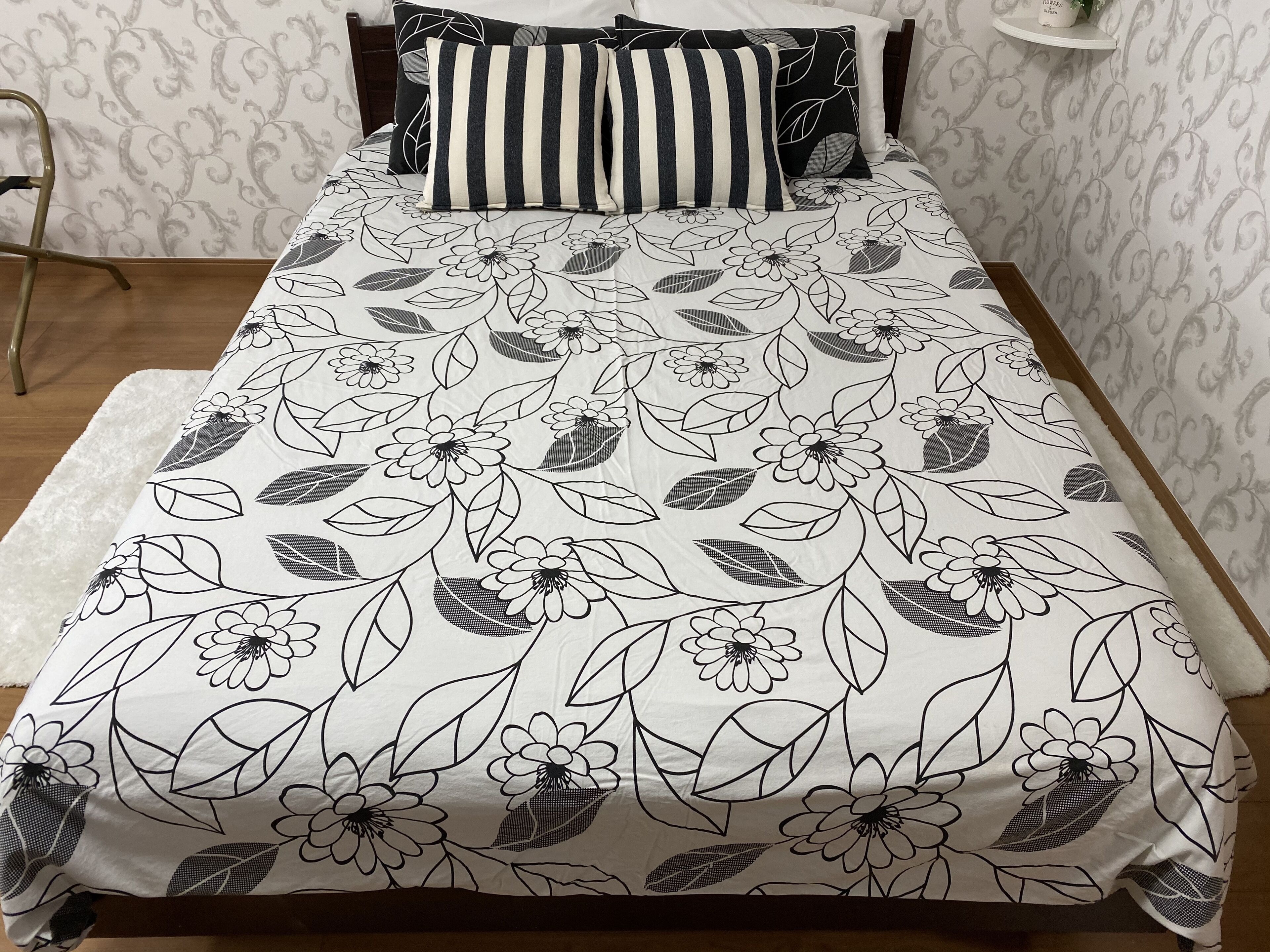 A bed with a floral-patterned bedspread, striped pillows, and a white nightstand with a plant.