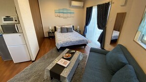 A compact hotel room with a bed, a sofa, a small kitchenette, and a window with curtains. - Beach House 1 & Private Beach (Onna)