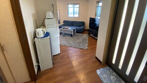 A compact living space with a kitchenette, a sofa, a television, and a window providing natural light. - Beach House 1 & Private Beach (Onna)