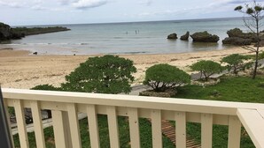 A beach view from a balcony with a railing, featuring a sandy beach, green shrubs, and a calm sea. - Beach House 1 & Private Beach (Onna)
