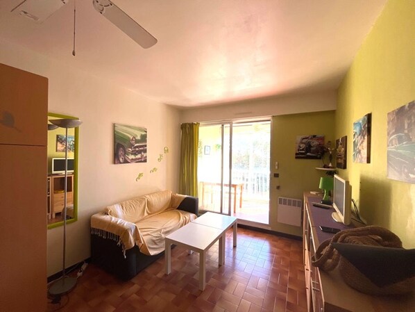 A living room with a sofa, a table, a TV, and a window with curtains.