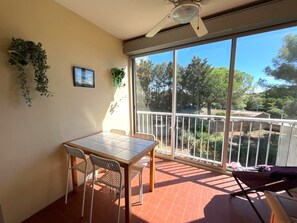A balcony with a table and chairs, a ceiling fan, and a view of trees and a house.