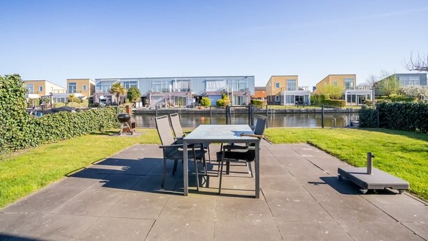 En uteplats med ett bord och stolar, en grill och utsikt över moderna byggnader och en kanal.