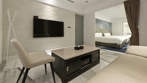 A modern hotel room with a flat-screen TV mounted on a white brick wall, a bed with white linens, a sofa, and a coffee table. - Fengjia Gold Hotel (Taichung)