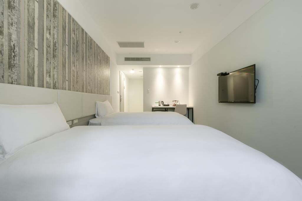 A modern hotel room with a large bed, a flat-screen TV mounted on the wall, and a minimalist design.