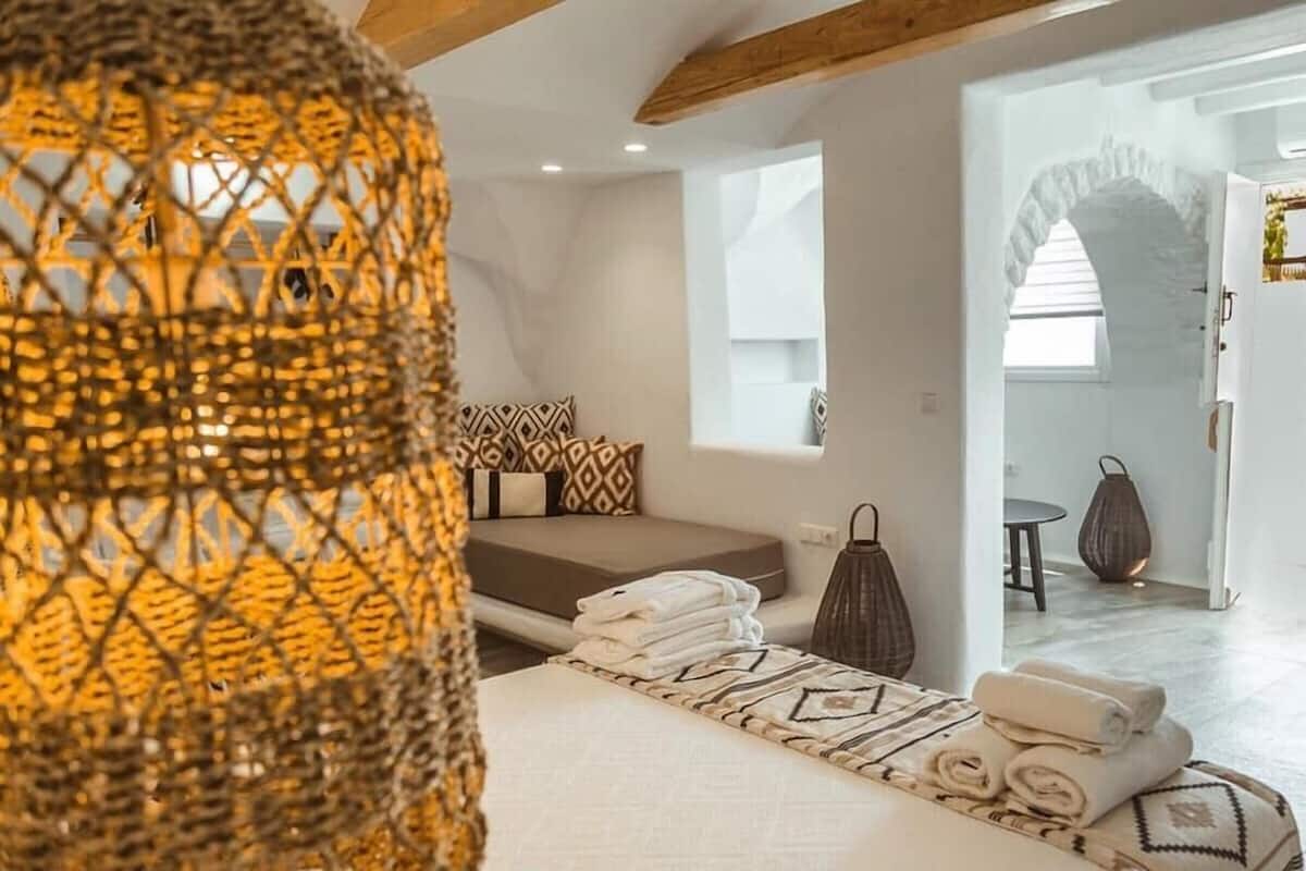 A modern bedroom with a bed, a small seating area, and a view of the adjacent room.