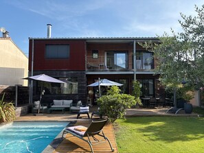 A modern two-story house with a swimming pool, outdoor seating, and a garden.
