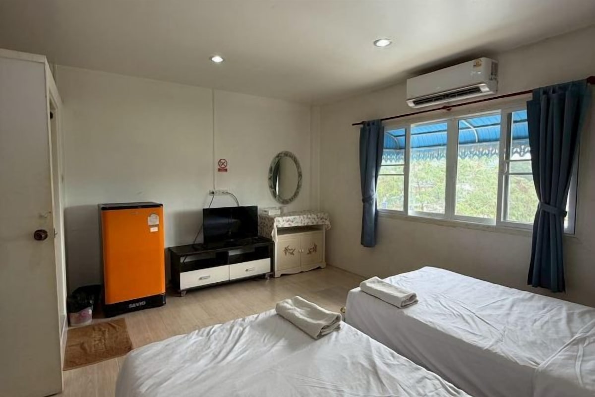 Ett hotellrum med en säng, en tv, ett litet kylskåp, en byrå och ett fönster med gardiner.