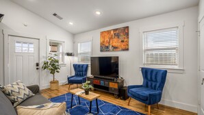 A modern living room with a flat-screen TV, two blue armchairs, a grey sofa, and a wooden coffee table.