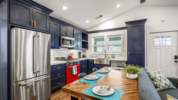 A modern kitchen with dark blue cabinets, stainless steel appliances, and a wooden dining table set for four.