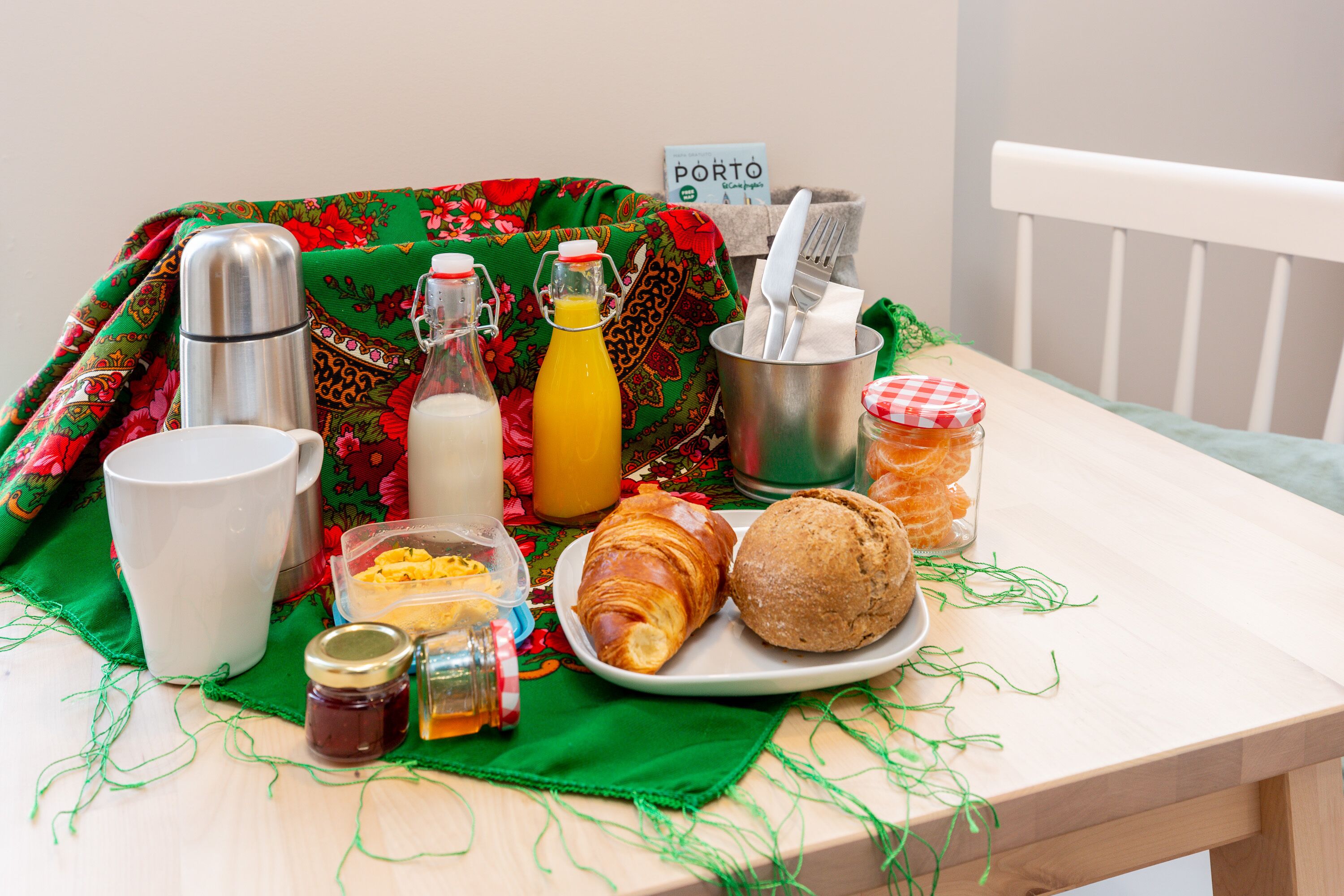 A breakfast table with a plate of food, a thermos, a bottle of orange juice, a jar of jam, and a sign that reads "PORTO".