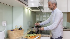 Uma cozinha moderna com alguém cozinhando, um bloco de madeira com garrafas e uma tábua de corte com legumes.